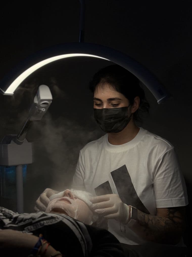 Aluna realizando limpeza de pele em modelo real, sob iluminação de estúdio, durante a aula prática