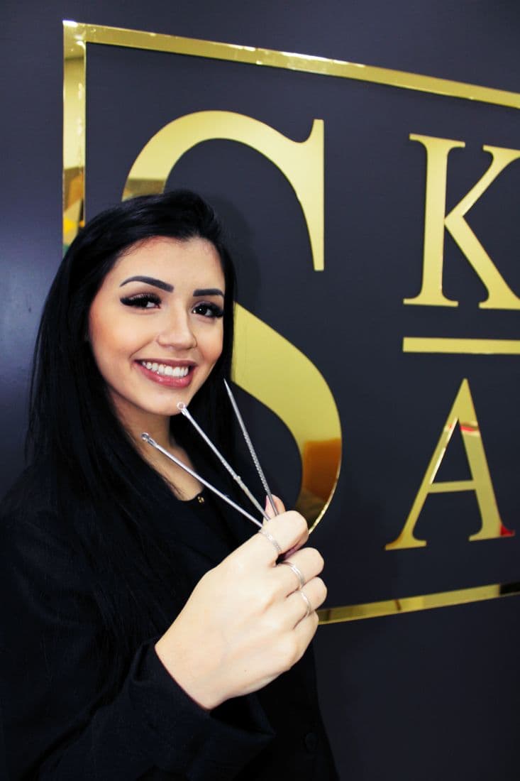 Kathleen Araújo segurando os extratores de limpeza de pele, em frente ao letreiro dourado do estúdio